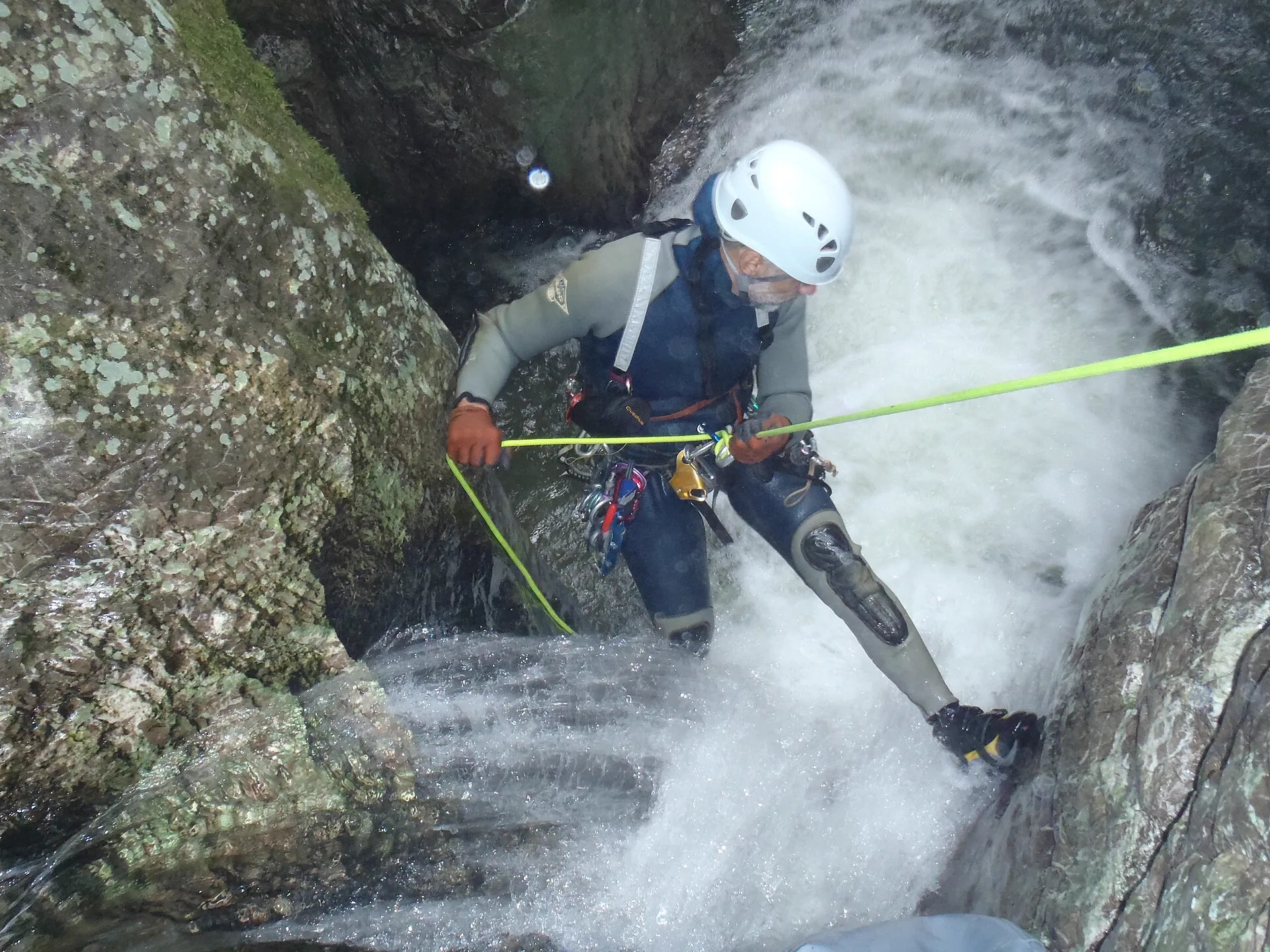 Canyoniste casqué et baudrier équipé en plein rappel dans une cascade